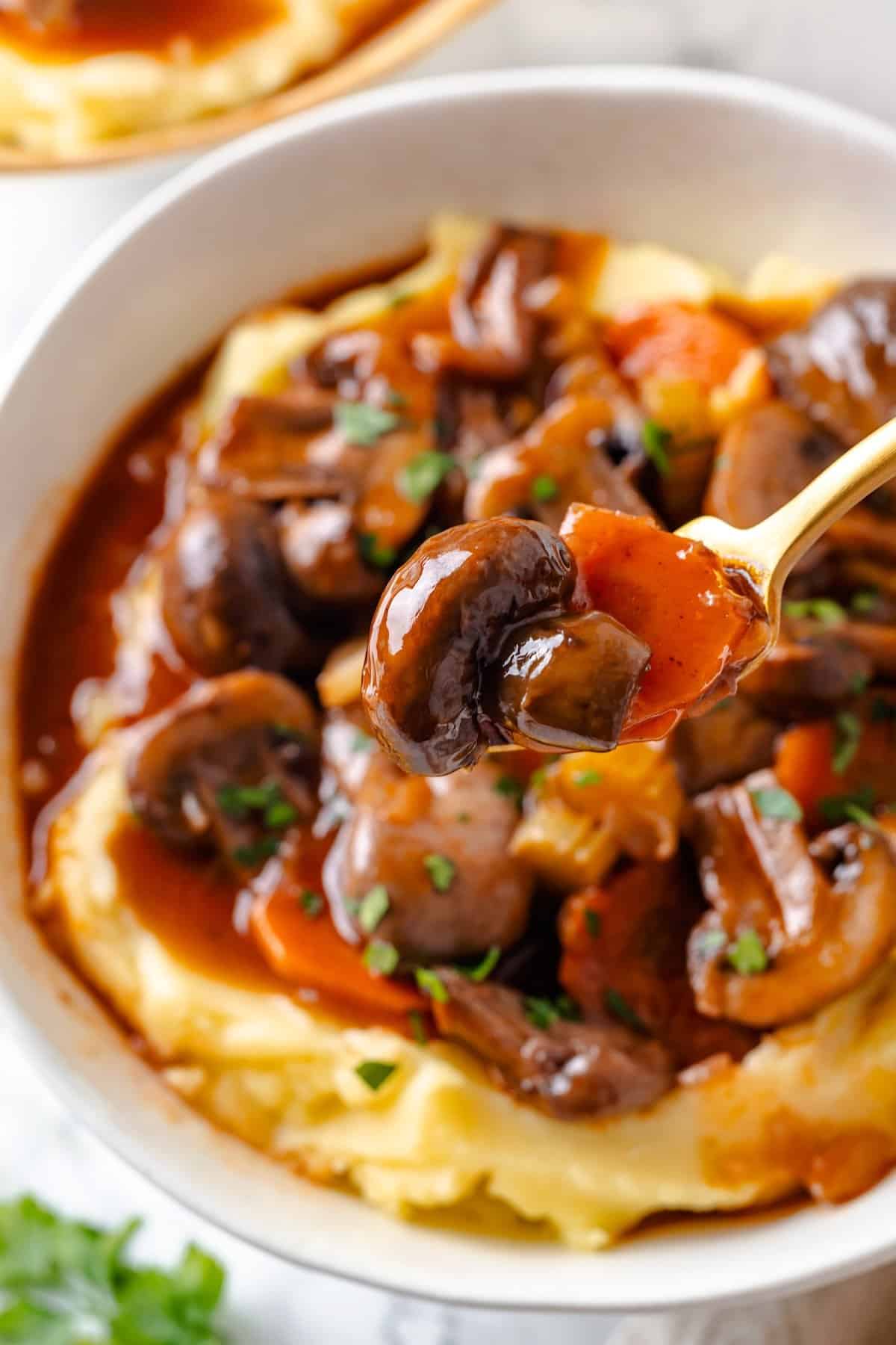 Mushroom bourguignon is a rich, savoury vegan stew simmered in red wine with herbs and meaty mushrooms. A cozy yet elegant meal! Spoonful of mushroom bourguignon held over bowl.