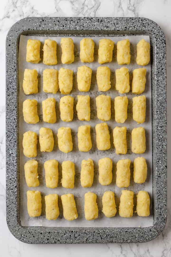 These homemade tater tots are crispy outside, fluffy inside and made with real potatoes. Bake, fry, air fry or freeze them for later! Tater tots lined up on baking sheet before cooking.