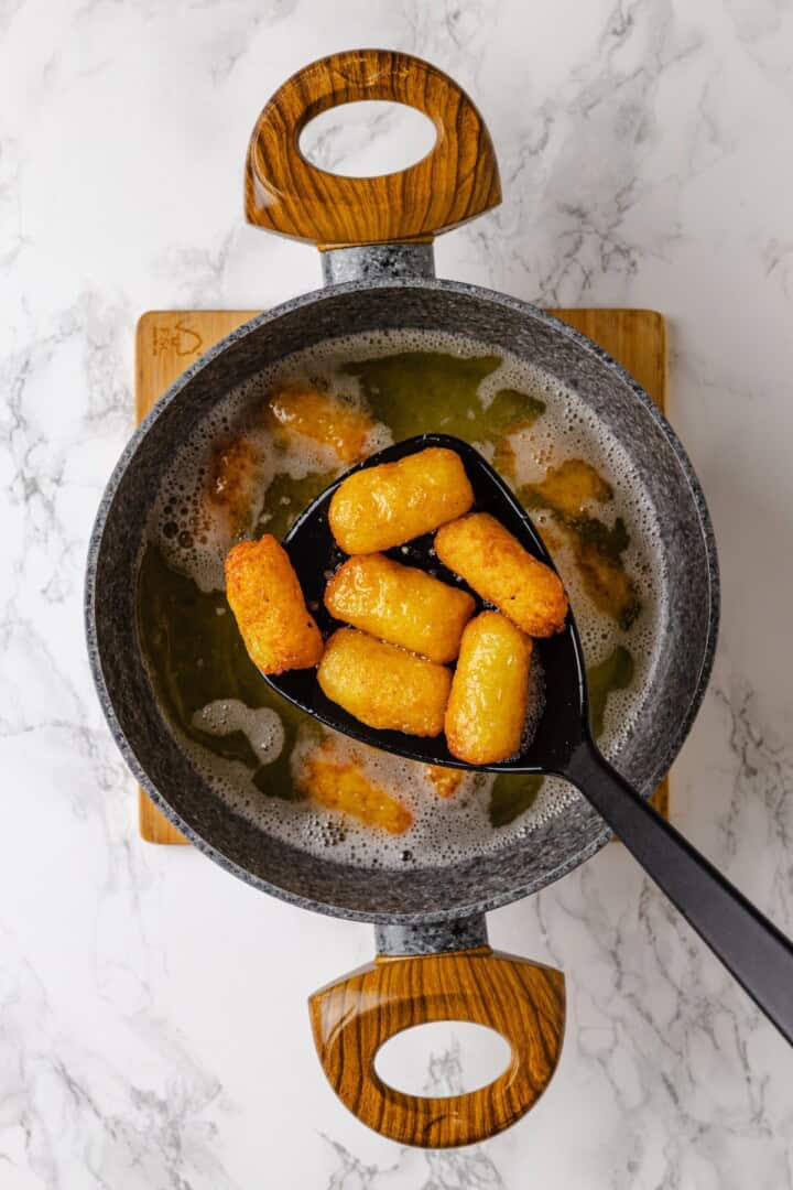 These homemade tater tots are crispy outside, fluffy inside and made with real potatoes. Bake, fry, air fry or freeze them for later! Removing tater tots from pot of oil.