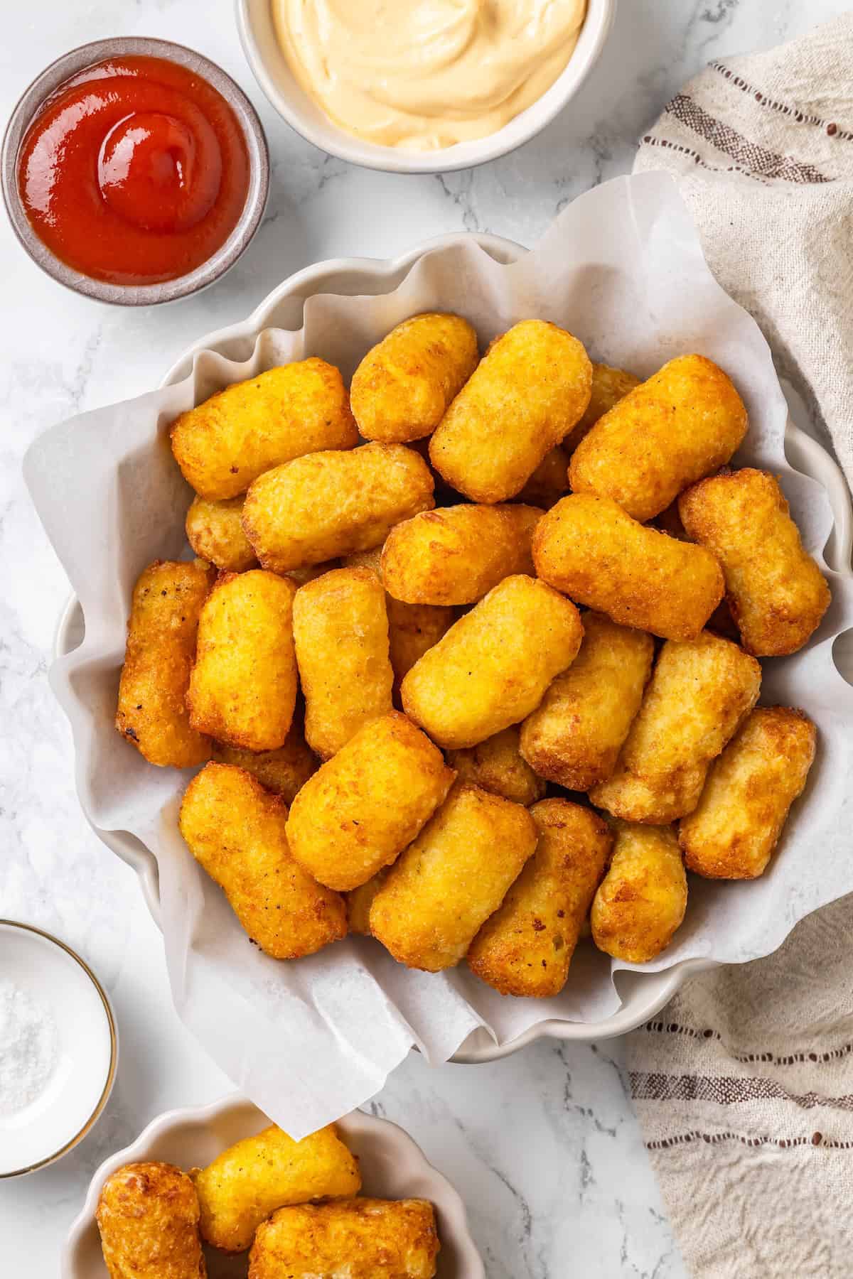 These homemade tater tots are crispy outside, fluffy inside and made with real potatoes. Bake, fry, air fry or freeze them for later! Bowl of crispy homemade tater tots with bowl of ketchup.