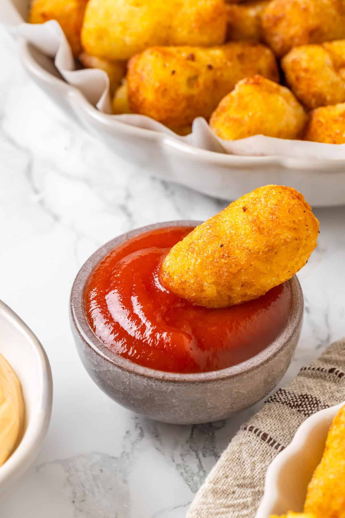 These homemade tater tots are crispy outside, fluffy inside and made with real potatoes. Bake, fry, air fry or freeze them for later! Homemade tater tot dipping into ketchup.