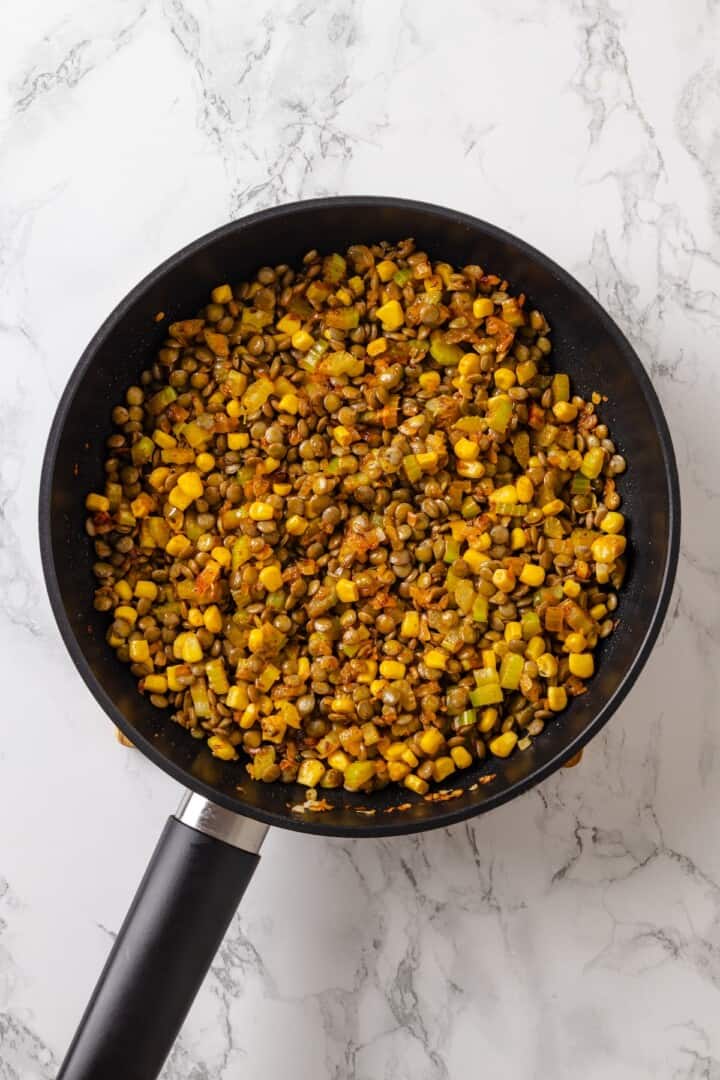 This vegan tater tot casserole recipe is creamy, hearty and topped with crispy homemade tots. A cozy, crowd-pleasing comfort food dinner! Lentils and vegetables in skillet.