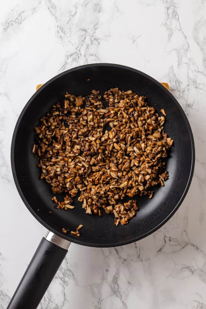 This vegan tater tot casserole recipe is creamy, hearty and topped with crispy homemade tots. A cozy, crowd-pleasing comfort food dinner! Browned mushrooms in skillet.