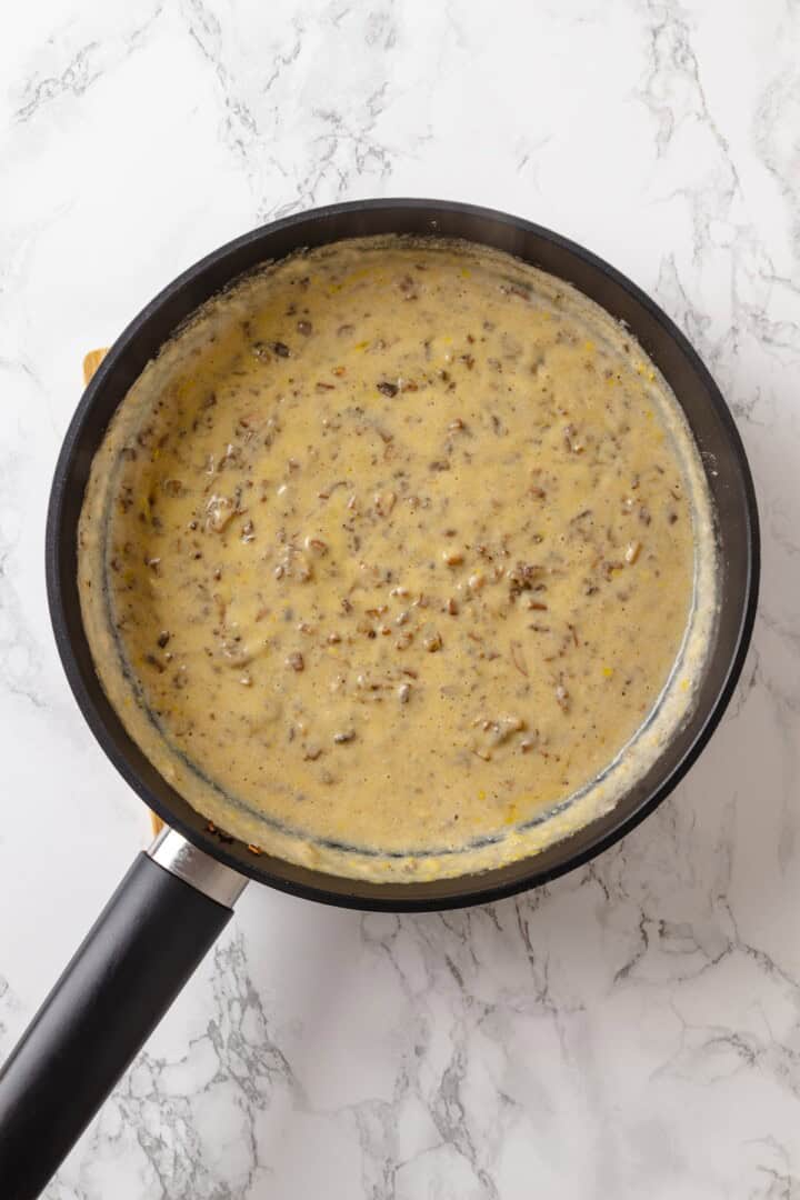 This vegan tater tot casserole recipe is creamy, hearty and topped with crispy homemade tots. A cozy, crowd-pleasing comfort food dinner! Creamy mushroom sauce in pan.