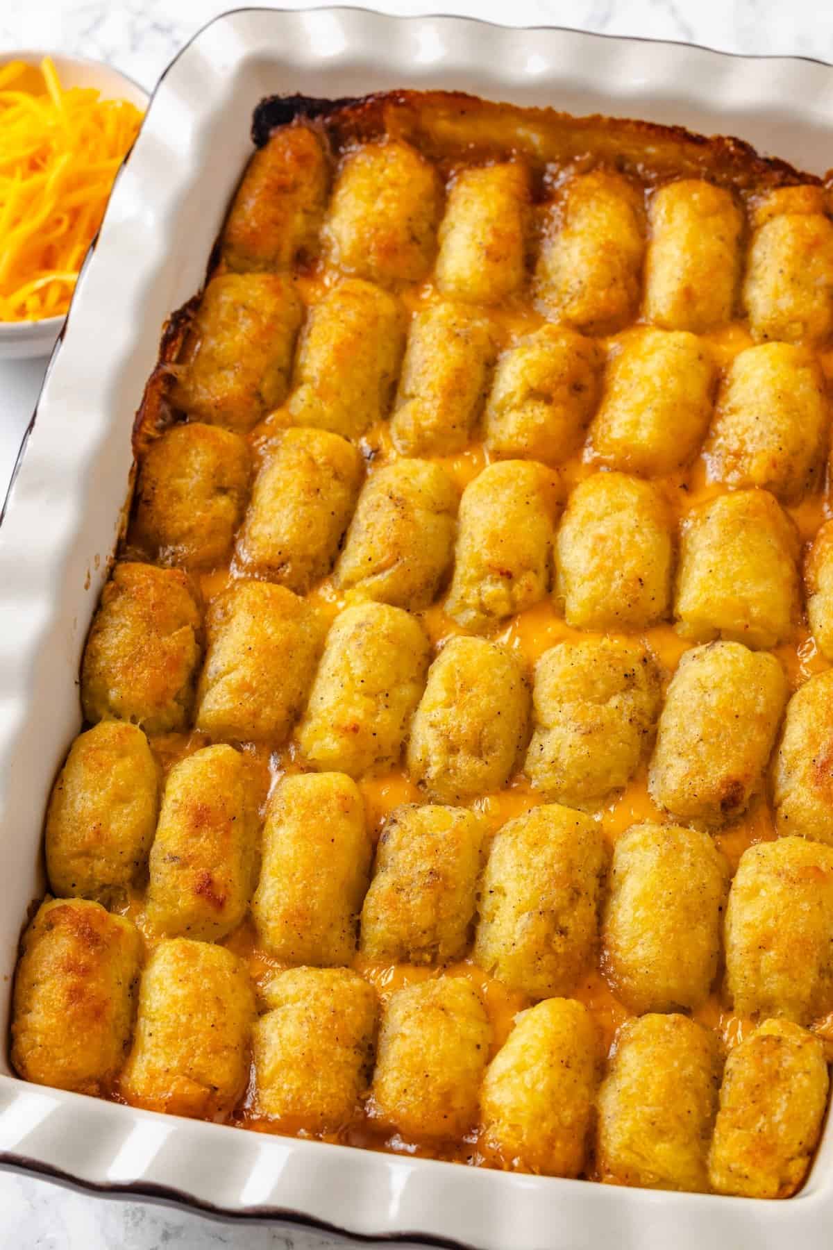 This vegan tater tot casserole recipe is creamy, hearty and topped with crispy homemade tots. A cozy, crowd-pleasing comfort food dinner! Vegan tater tot casserole in baking dish.