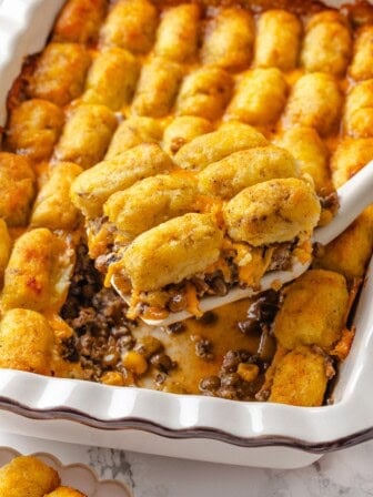 Lifting portion of vegan tater tot casserole from pan.