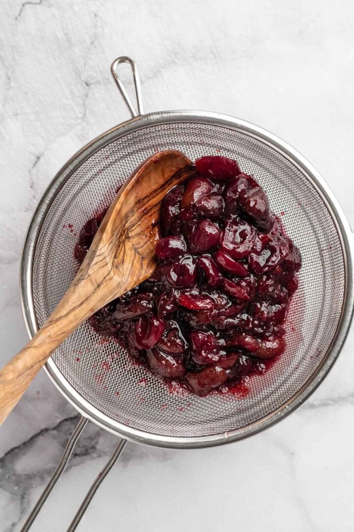 Mashing cherries in sieve.