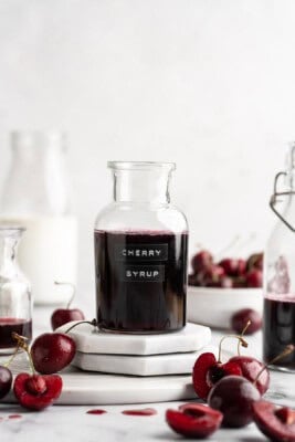 Bottle of cherry syrup with fresh cherries.