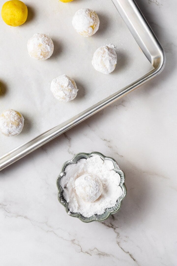 These vegan lemon crinkle cookies bake up soft and chewy, with a sunny citrus flavour and a classic powdered sugar crackle on top. Lovely! Lemon crinkle cookie dough in bowl of powdered sugar.