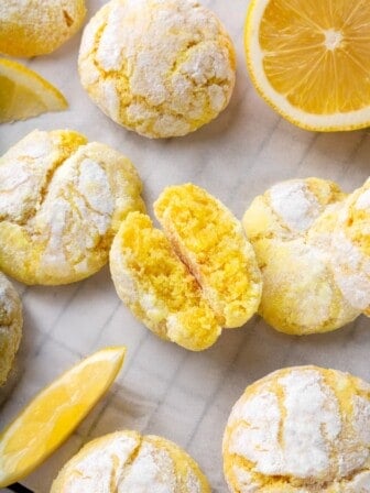 Lemon crinkle cookies on parchment paper with one cookie broken in half to show tender crumb.