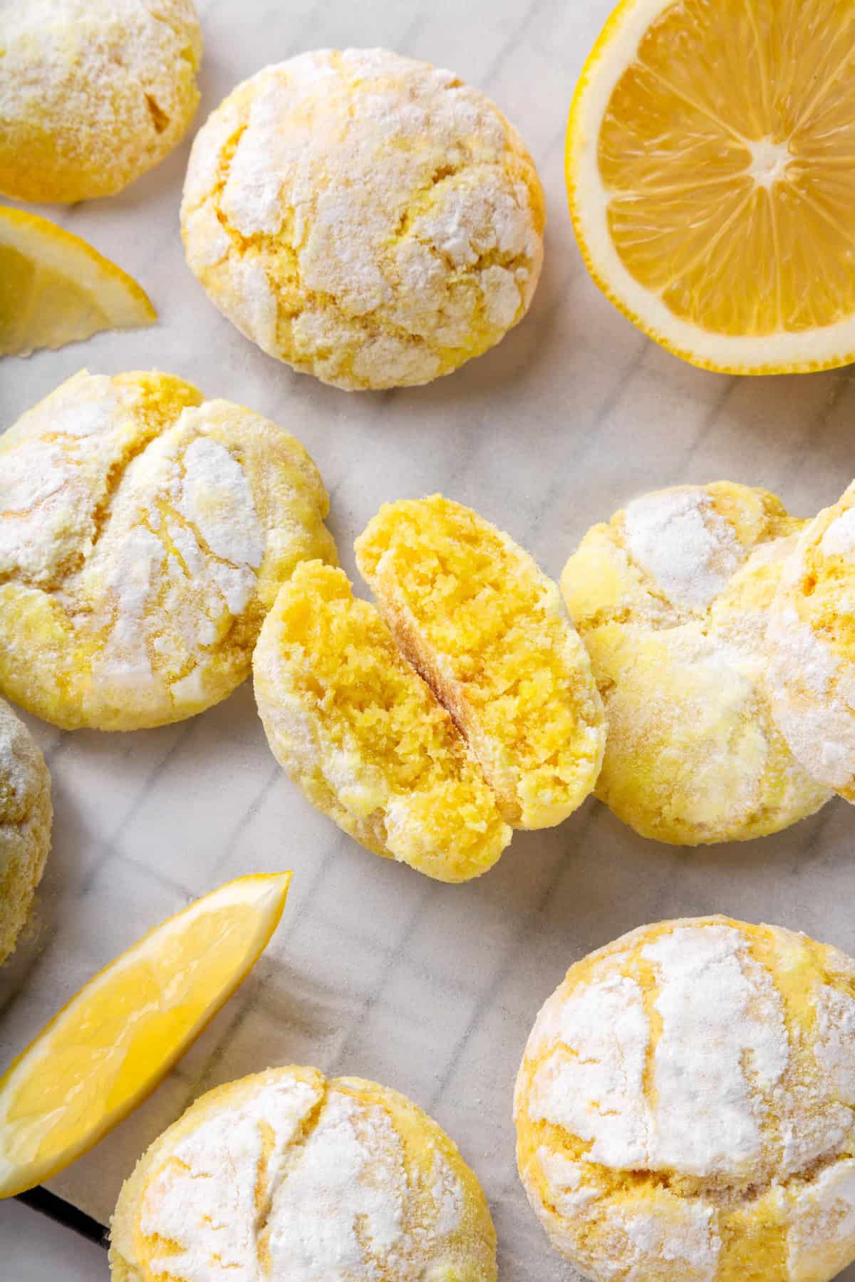 These vegan lemon crinkle cookies bake up soft and chewy, with a sunny citrus flavour and a classic powdered sugar crackle on top. Lovely! Lemon crinkle cookies on parchment paper with one cookie broken in half to show tender crumb.