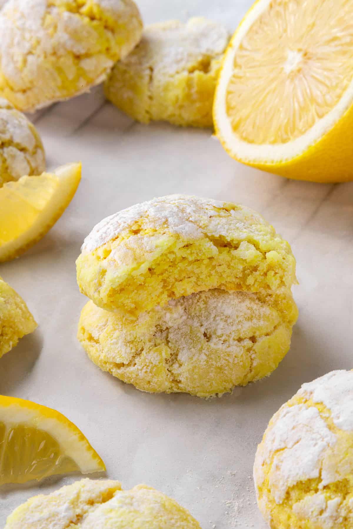 These vegan lemon crinkle cookies bake up soft and chewy, with a sunny citrus flavour and a classic powdered sugar crackle on top. Lovely! Two stacked lemon crinkle cookies, with top cookie bitten to show tender crumb.