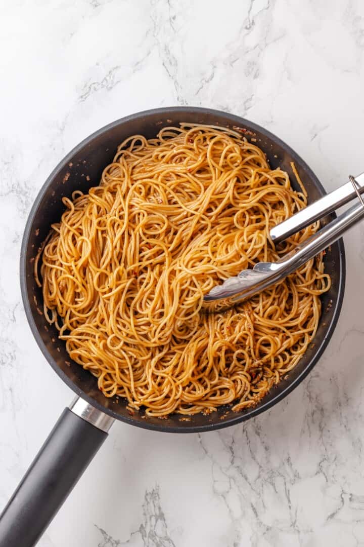 These vegan garlic noodles deliver bold, buttery garlic flavour in a quick, satisfying dish that’s ready in just 20 minutes! Tongs tossing garlic noodles in pan.
