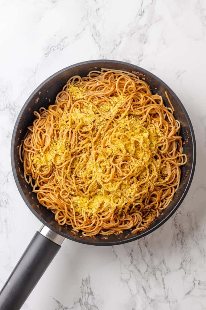 These vegan garlic noodles deliver bold, buttery garlic flavour in a quick, satisfying dish that’s ready in just 20 minutes! Nutritional yeast added to vegan garlic noodles in skillet.