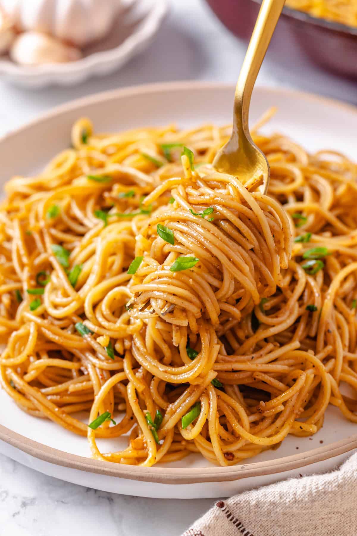 These vegan garlic noodles deliver bold, buttery garlic flavour in a quick, satisfying dish that’s ready in just 20 minutes! Garlic noodles twirled around fork held over plate.