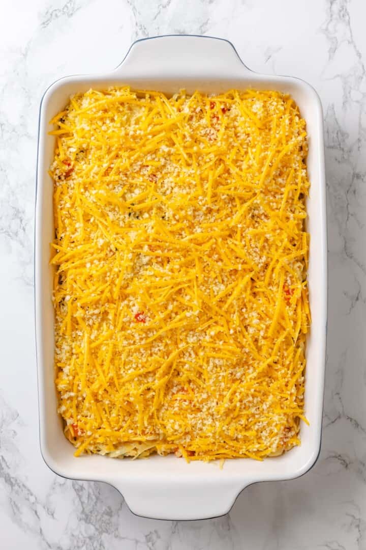 Loaded hashbrown casserole topped with cheese before baking.