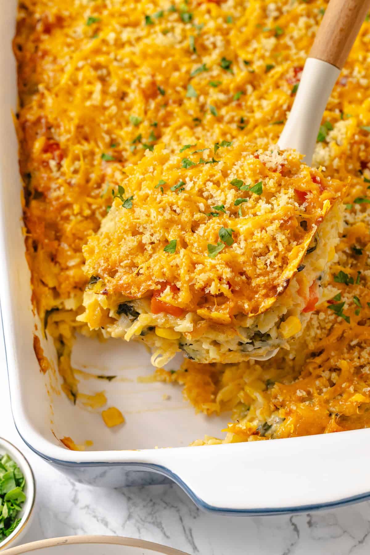 Lifting portion of loaded hashbrown casserole from dish.