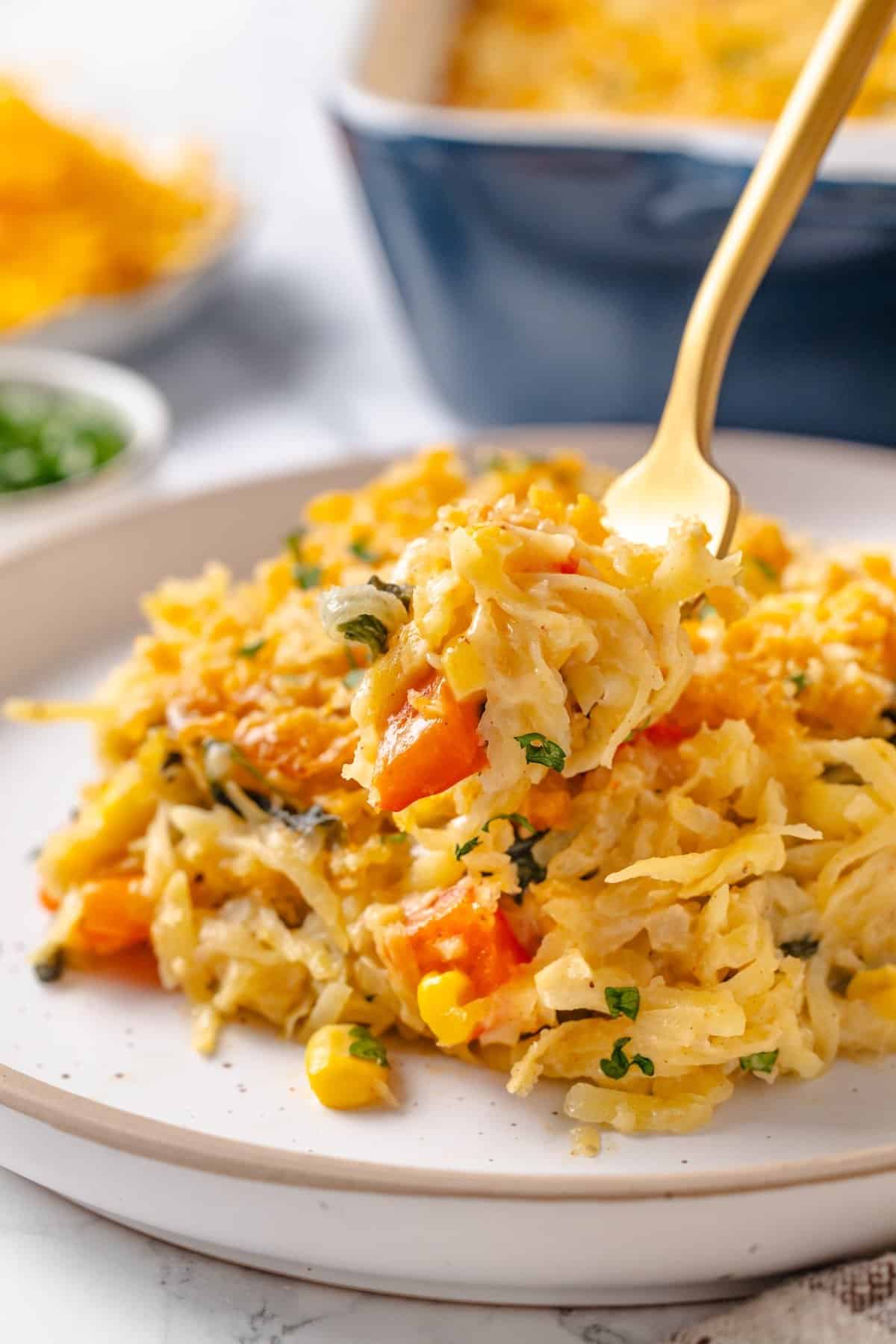 Forkful of loaded hashbrown casserole held over plate.