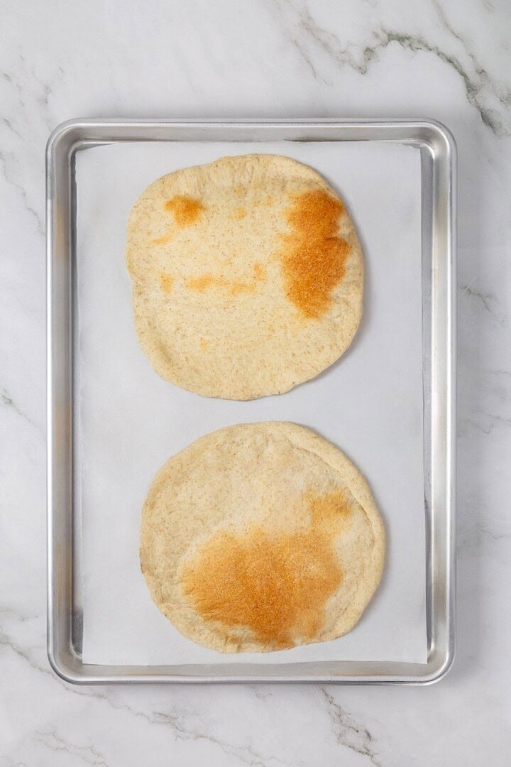 Tender and warm, with a perfect pocket in the middle, this easy homemade pita bread recipe gives your wraps, dips and sandwiches an upgrade! Two homemade pitas on parchment lined pan.
