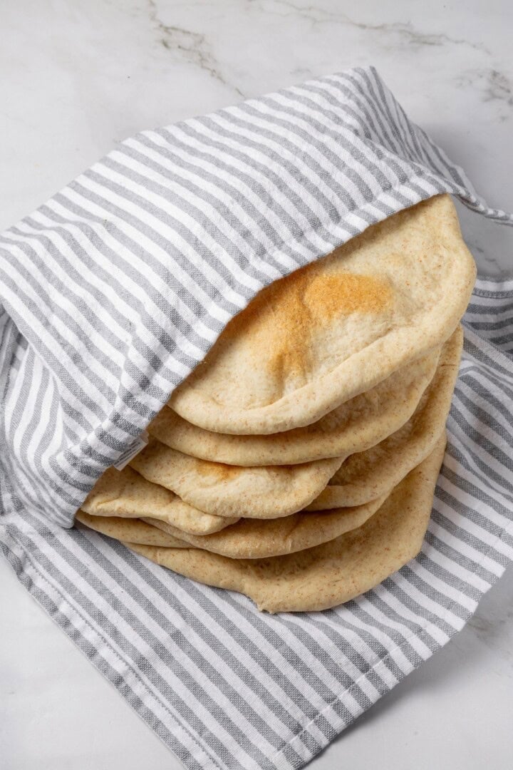 Tender and warm, with a perfect pocket in the middle, this easy homemade pita bread recipe gives your wraps, dips and sandwiches an upgrade! Pita bread wrapped in kitchen towel.