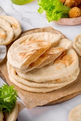 Stack of homemade pita bread with top piece sliced in half to show pocket.