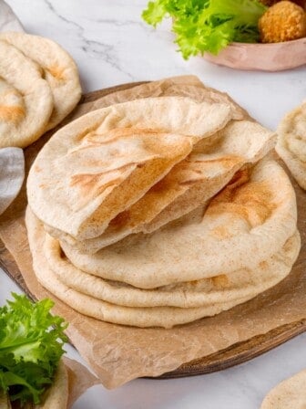 Stack of homemade pita bread with top piece sliced in half to show pocket.