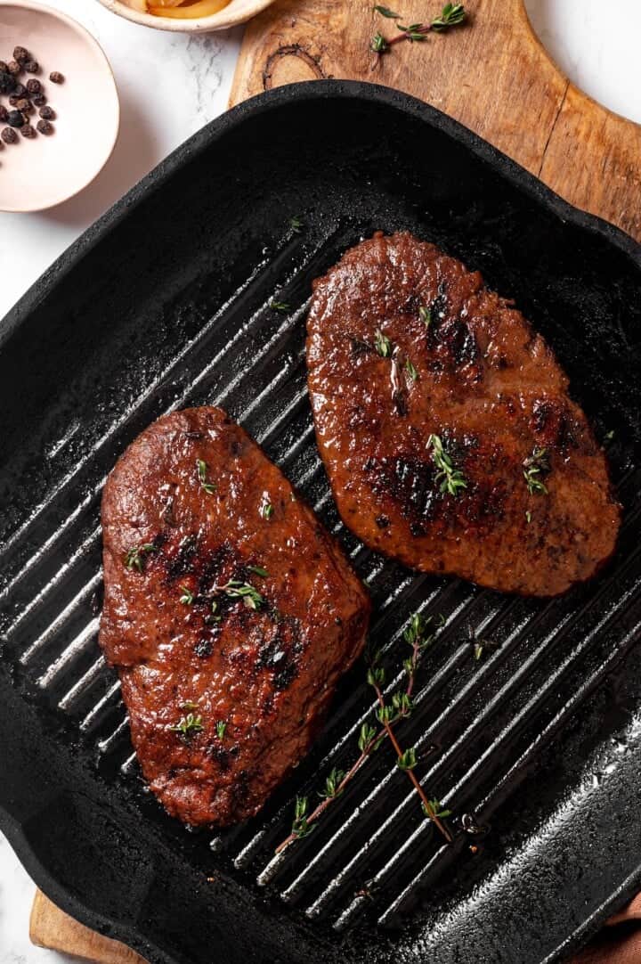 Savory, hearty and full of umami flavor, this homemade vegan steak is made with seitan for a protein-packed plant-based main dish! Two vegan steaks in grill pan with thyme.