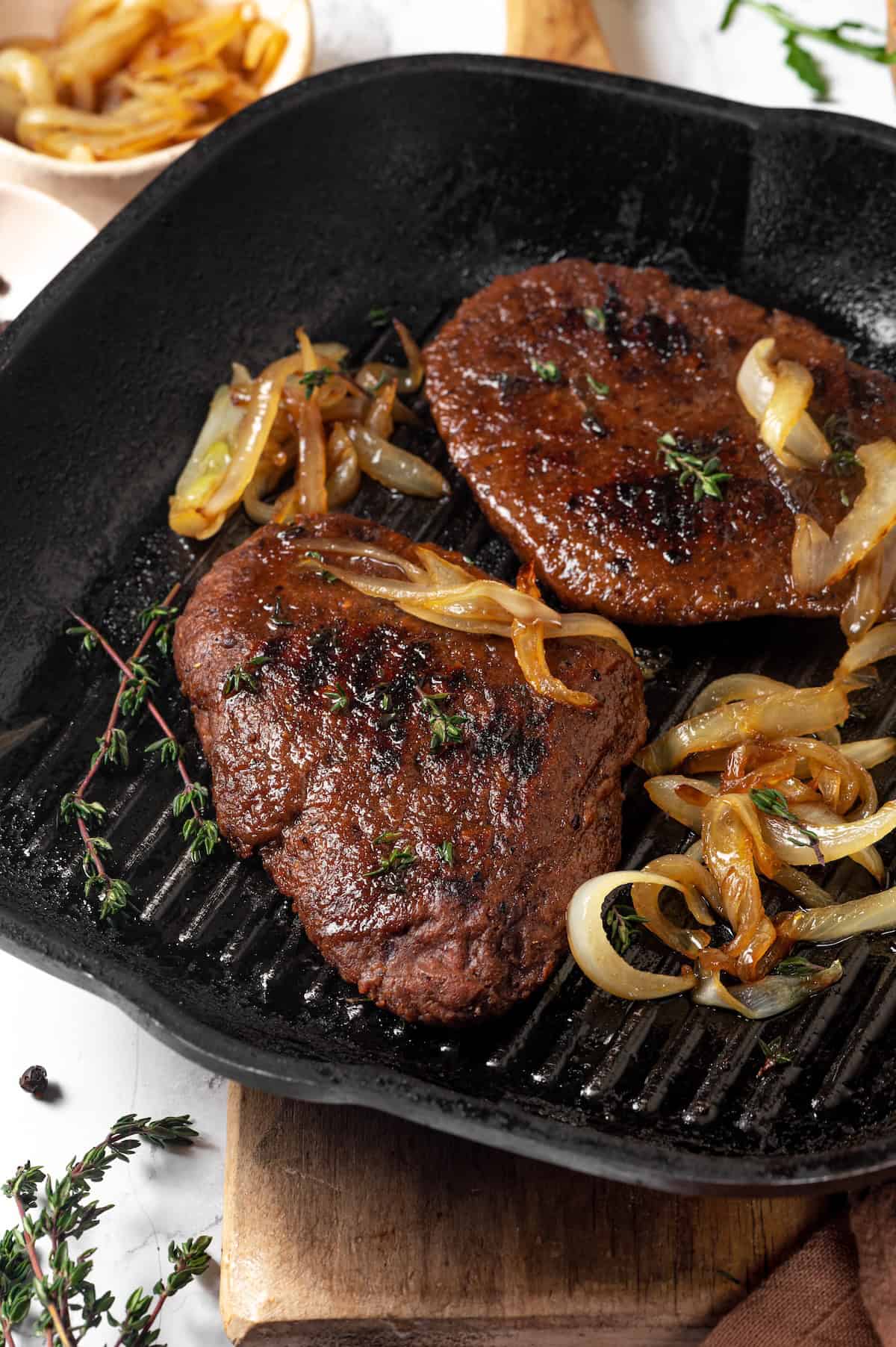 Savory, hearty and full of umami flavor, this homemade vegan steak is made with seitan for a protein-packed plant-based main dish! Vegan steaks in grill pan with caramelized onions.