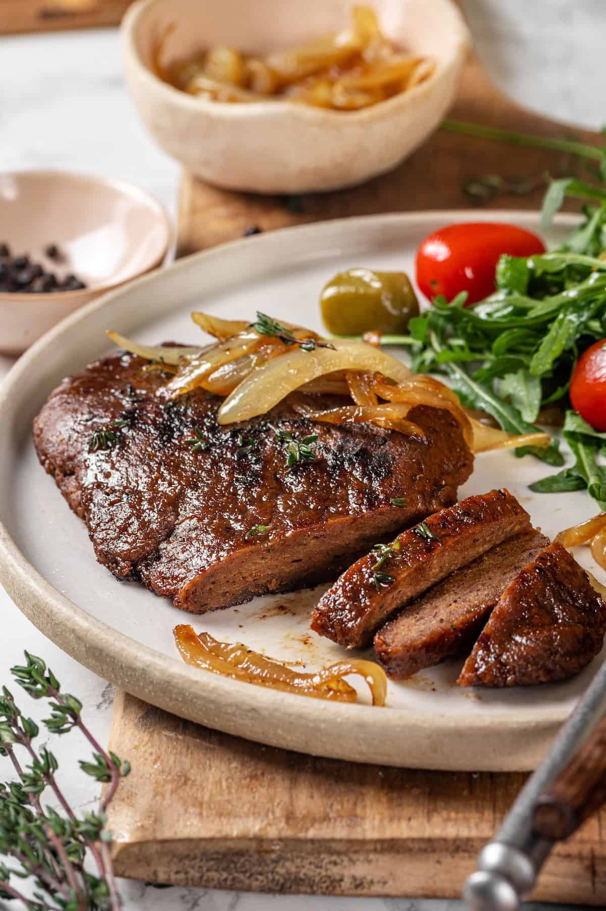Savory, hearty and full of umami flavor, this homemade vegan steak is made with seitan for a protein-packed plant-based main dish! Sliced vegan steak on plate with salad.