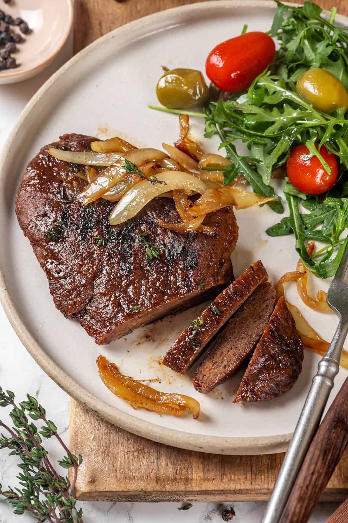 Savory, hearty and full of umami flavor, this homemade vegan steak is made with seitan for a protein-packed plant-based main dish! Vegan steak with caramelized onions on plate with salad.