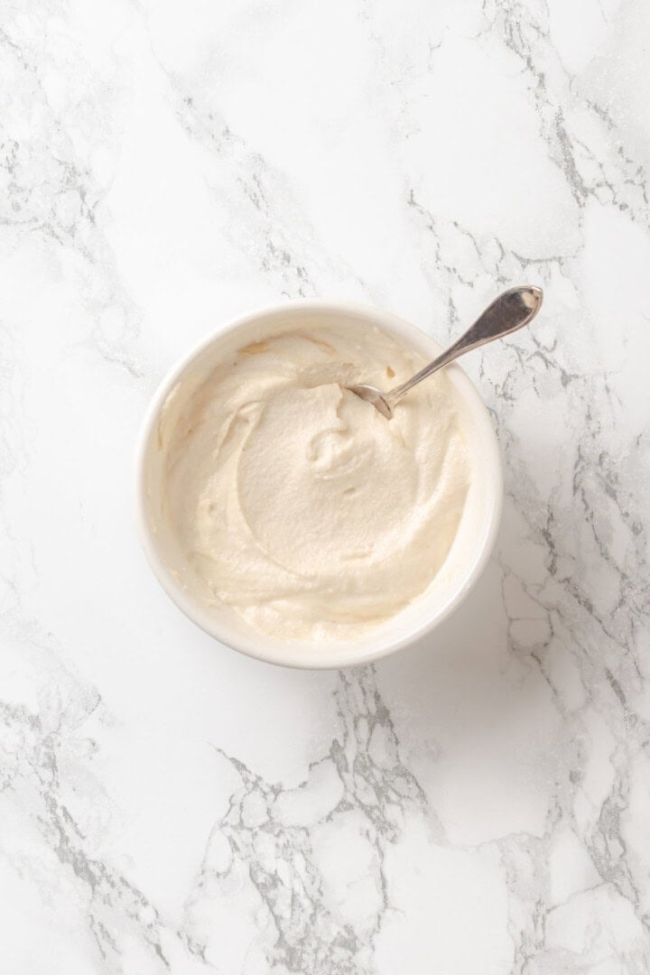 Golden, custardy, and filled with jammy berries and vanilla cream cheese, this vegan stuffed French toast turns brunch into something special! Bowl of cream cheese mixture with spoon.