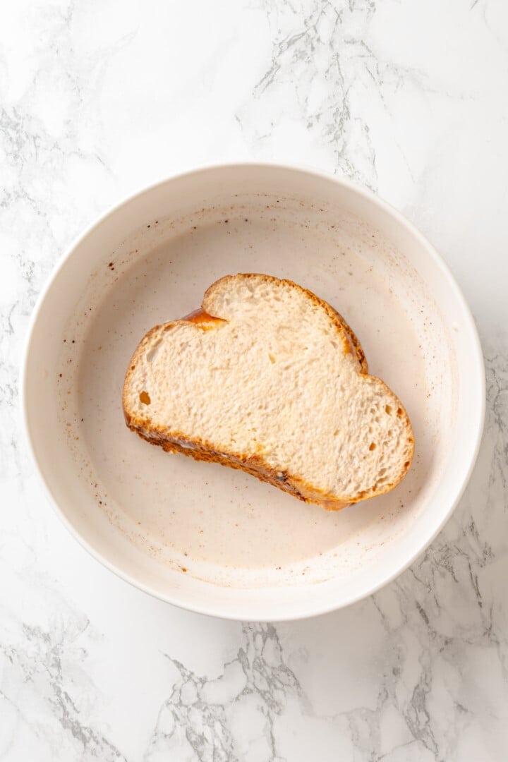 Golden, custardy, and filled with jammy berries and vanilla cream cheese, this vegan stuffed French toast turns brunch into something special! Slice of bread in bowl of custard.