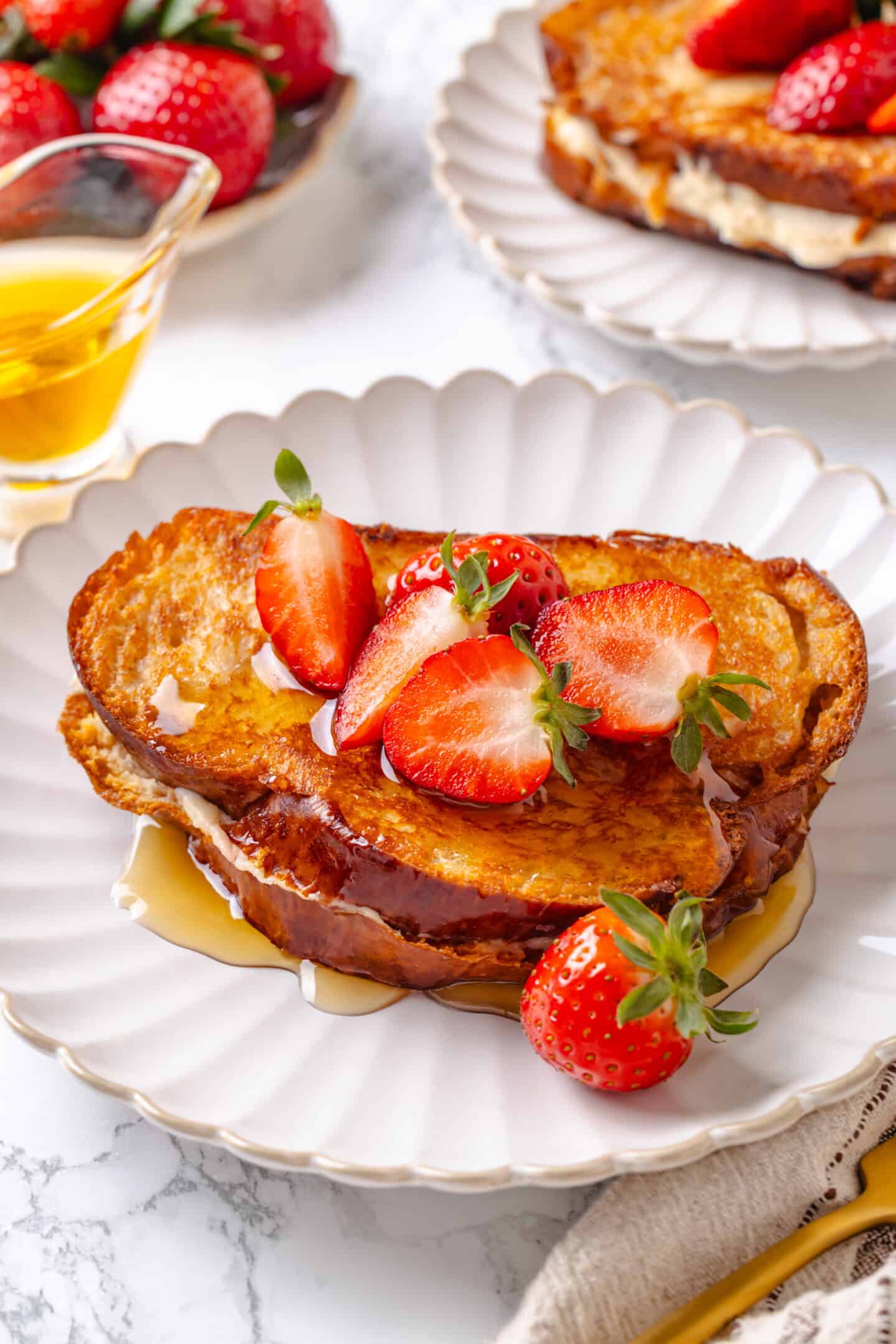 Golden, custardy, and filled with jammy berries and vanilla cream cheese, this vegan stuffed French toast turns brunch into something special! Strawberry stuffed French toast on plate with maple syrup.