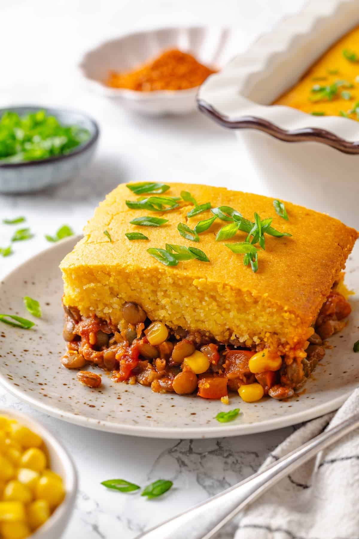 Tamale casserole portion on plate with green onions for garnish.