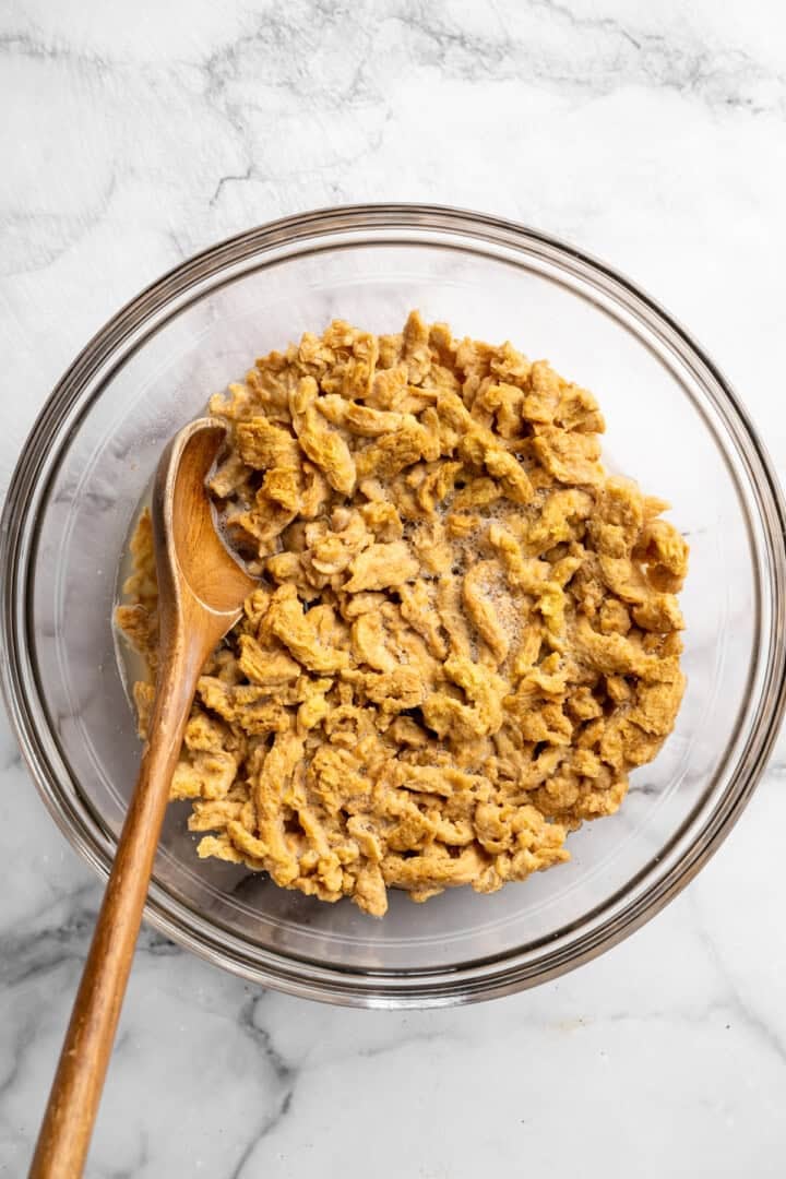 A little bit crispy, budget-friendly and packed with bold flavour, these BBQ soy curls are an easy vegan staple you’ll make again and again! Stirring soy curls in bowl.