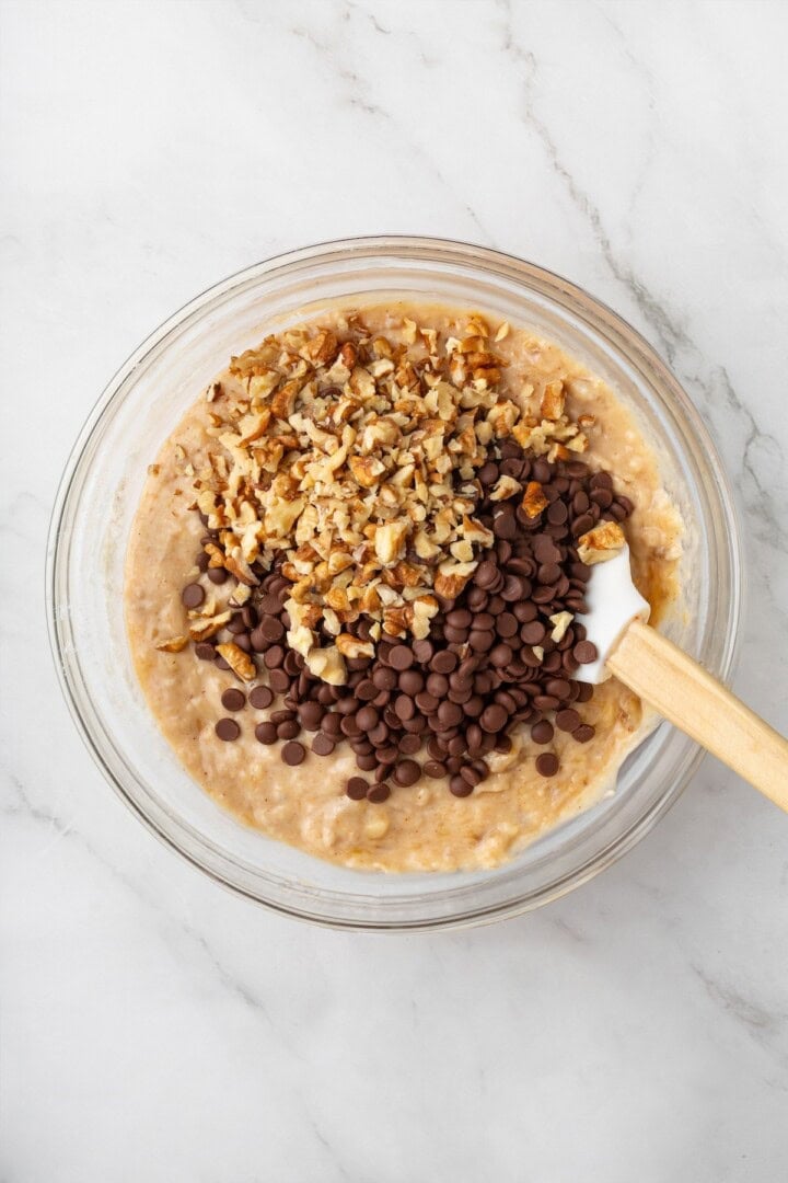 These vegan banana chocolate chip muffins bake up soft, moist and full of chocolate and crunchy walnuts. Perfect for breakfast and snacks! Stirring chocolate chips and walnuts into banana muffin batter.