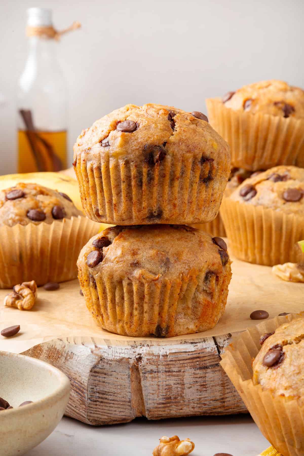 These vegan banana chocolate chip muffins bake up soft, moist and full of chocolate and crunchy walnuts. Perfect for breakfast and snacks! Stack of 2 banana chocolate chip muffins on board.