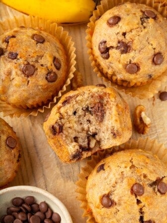Vegan banana chocolate chip muffins on wooden board with one bitten into to show texture.