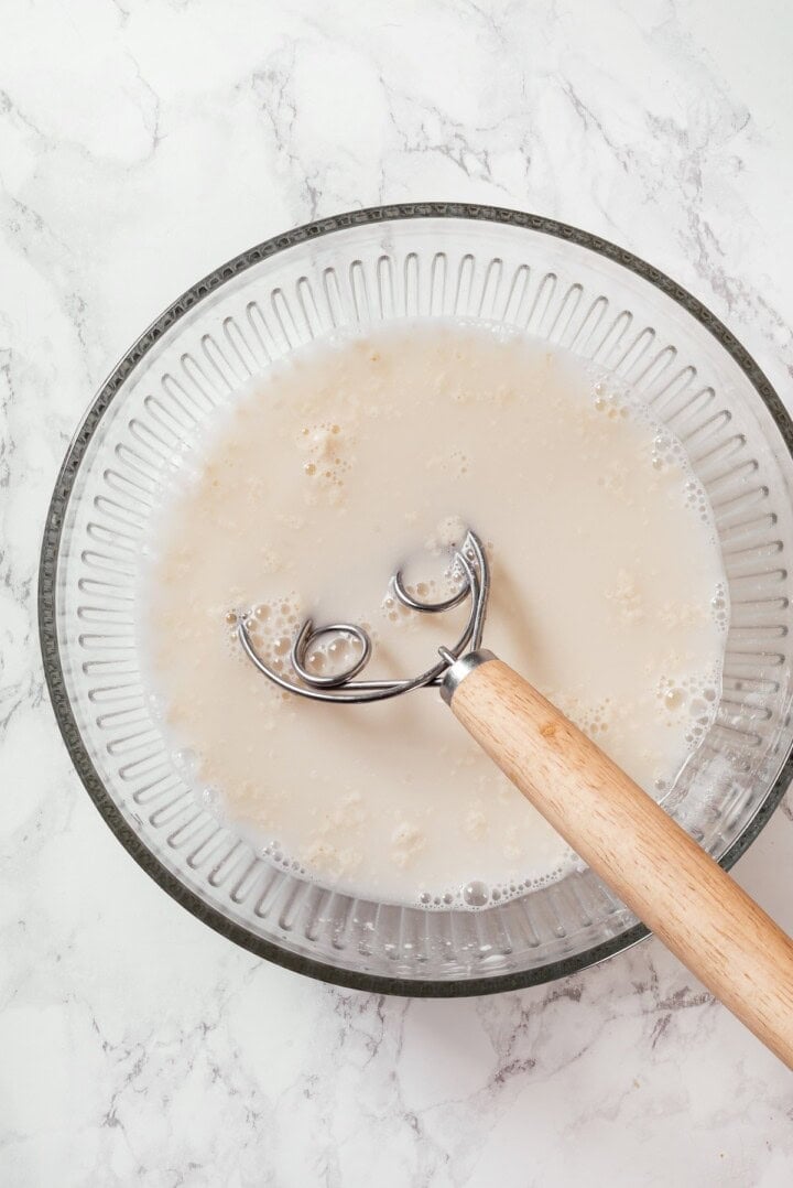 This Dutch oven sourdough bread gives you a bakery-style loaf with a crisp, golden crust and chewy interior. It's easier than you think! Bread whisk in bowl of sourdough bread ingredients.