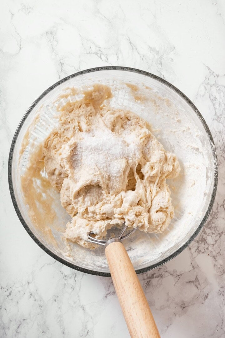 This Dutch oven sourdough bread gives you a bakery-style loaf with a crisp, golden crust and chewy interior. It's easier than you think! Dough whisk in bowl with ingredients for Dutch oven sourdough bread.