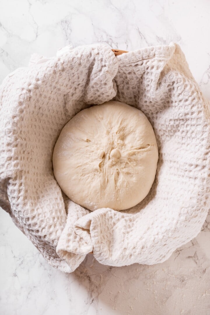This Dutch oven sourdough bread gives you a bakery-style loaf with a crisp, golden crust and chewy interior. It's easier than you think! Sourdough loaf in towel-lined bowl.