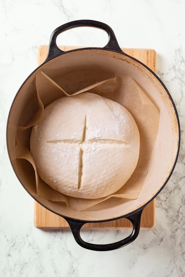 This Dutch oven sourdough bread gives you a bakery-style loaf with a crisp, golden crust and chewy interior. It's easier than you think! Unbaked loaf of sourdough bread in Dutch oven.