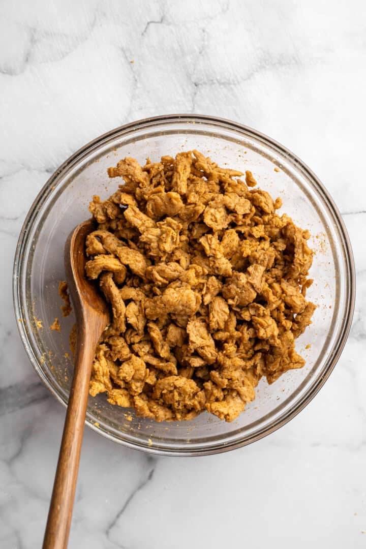 Soy curl "chicken" is a budget-friendly vegan swap for chicken that's crispy on the outside, full of savoury flavour, and super versatile! Stirring soy curls in bowl with seasonings.
