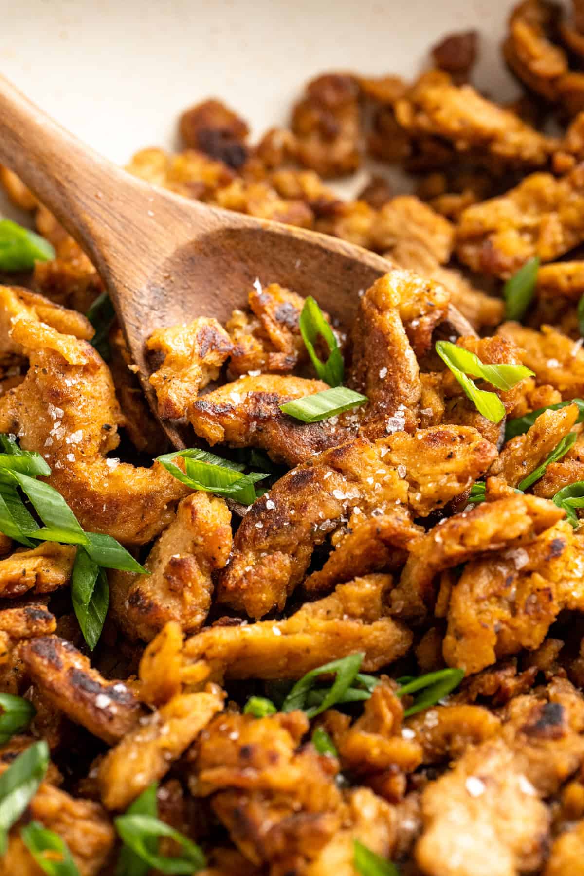 Soy curl "chicken" is a budget-friendly vegan swap for chicken that's crispy on the outside, full of savoury flavour, and super versatile! Stirring soy curl chicken with wooden spoon.