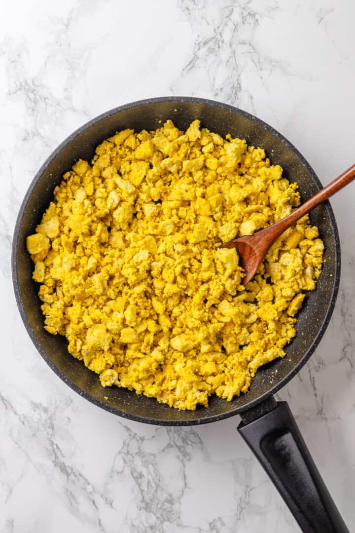 This vegan breakfast crunchwrap layers a crispy tortilla with tofu scramble, vegan bacon and creamy jalapeño sauce for a satisfying breakfast! Skillet of tofu scramble with wooden spoon.