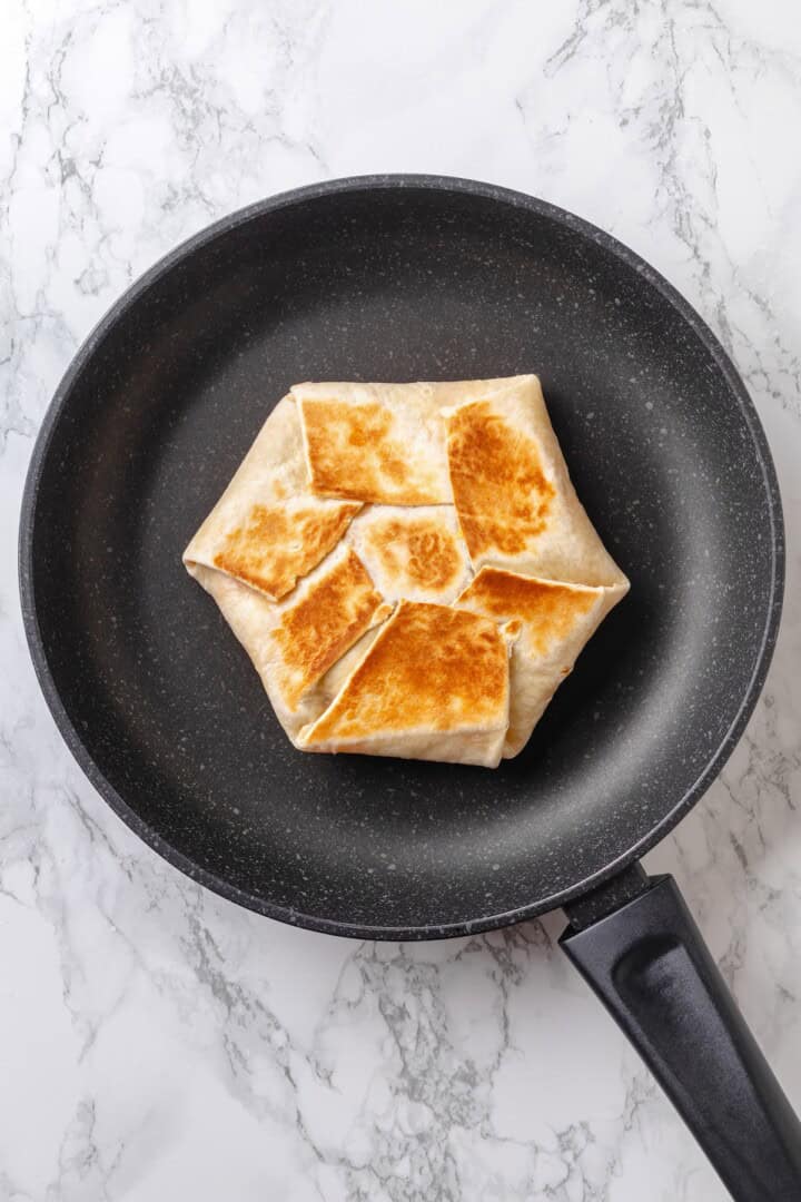 This vegan breakfast crunchwrap layers a crispy tortilla with tofu scramble, vegan bacon and creamy jalapeño sauce for a satisfying breakfast! Toasting breakfast crunchwrap in skillet.