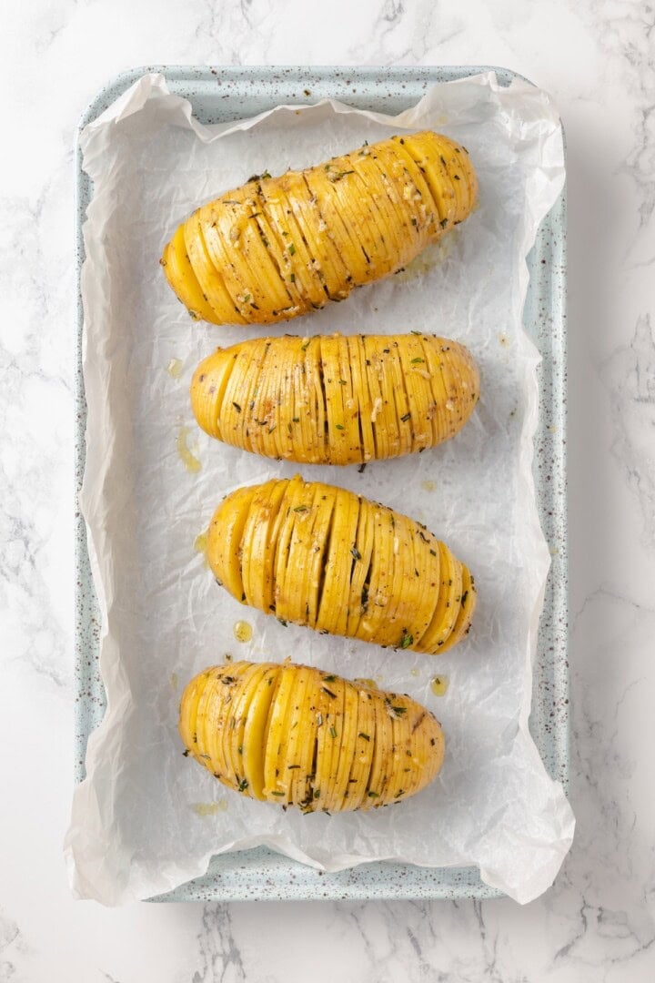 Hasselback potatoes are perfect for a party! The edges get crispy, the insides are tender, and garlic herb butter makes them irresistible. Sliced hasselback potatoes on pan before baking.