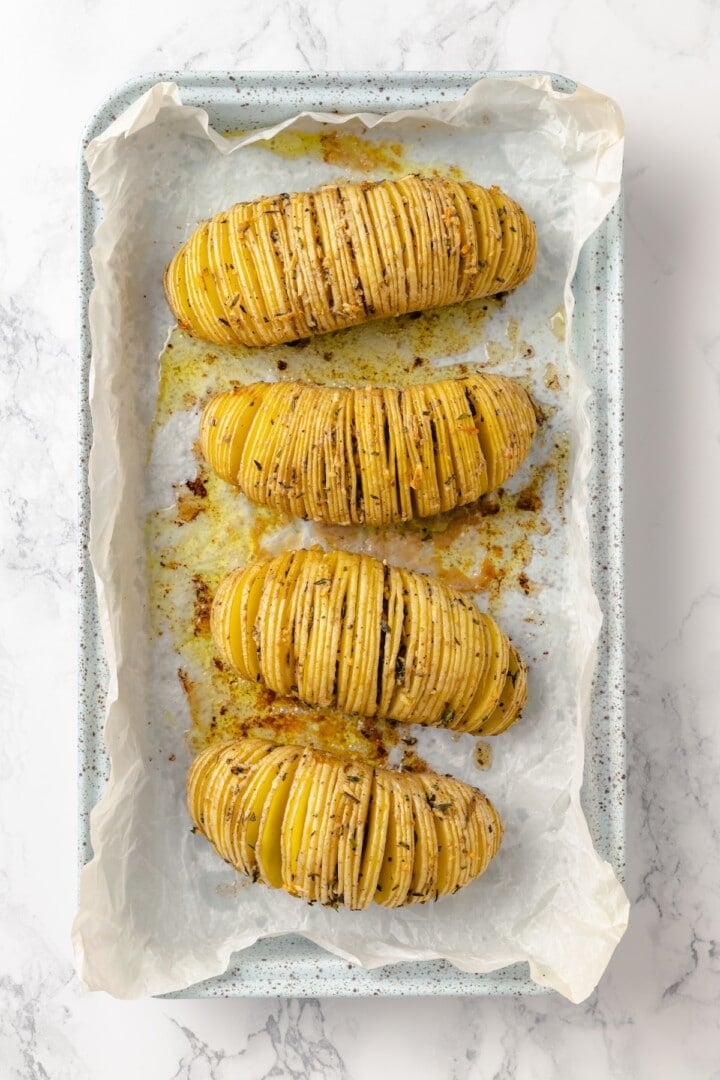 Hasselback potatoes are perfect for a party! The edges get crispy, the insides are tender, and garlic herb butter makes them irresistible. 4 hasselback potatoes on sheet pan before finishing.