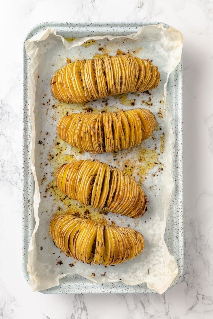 Hasselback potatoes are perfect for a party! The edges get crispy, the insides are tender, and garlic herb butter makes them irresistible. 4 hasselback potatoes on sheet pan before adding parsley.