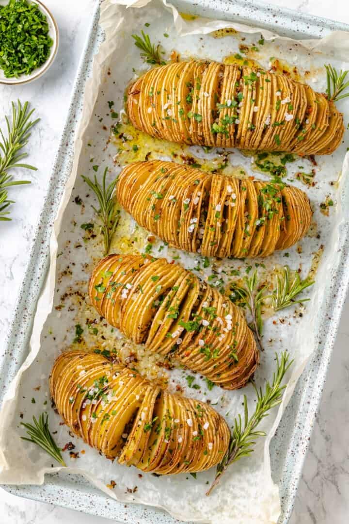 Hasselback potatoes are perfect for a party! The edges get crispy, the insides are tender, and garlic herb butter makes them irresistible. 4 hasselback potatoes on sheet pan.